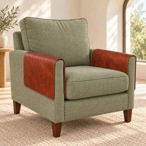May include: An armchair upholstered in sage green fabric featuring a large back cushion and a seat cushion. The armrests are accented with smooth, brown leather-like covers that wrap over the top and sides of the frame, supported by four dark wooden legs.