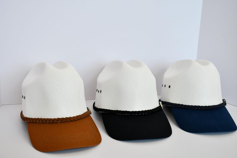 May include: Three white cowboy hats with different colored brims. The hats have a black braided band around the crown. The brims are brown, black, and navy blue.