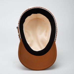 May include: A brown and black baseball cap with a white brim. The inside of the cap is lined with a cream-colored fabric.