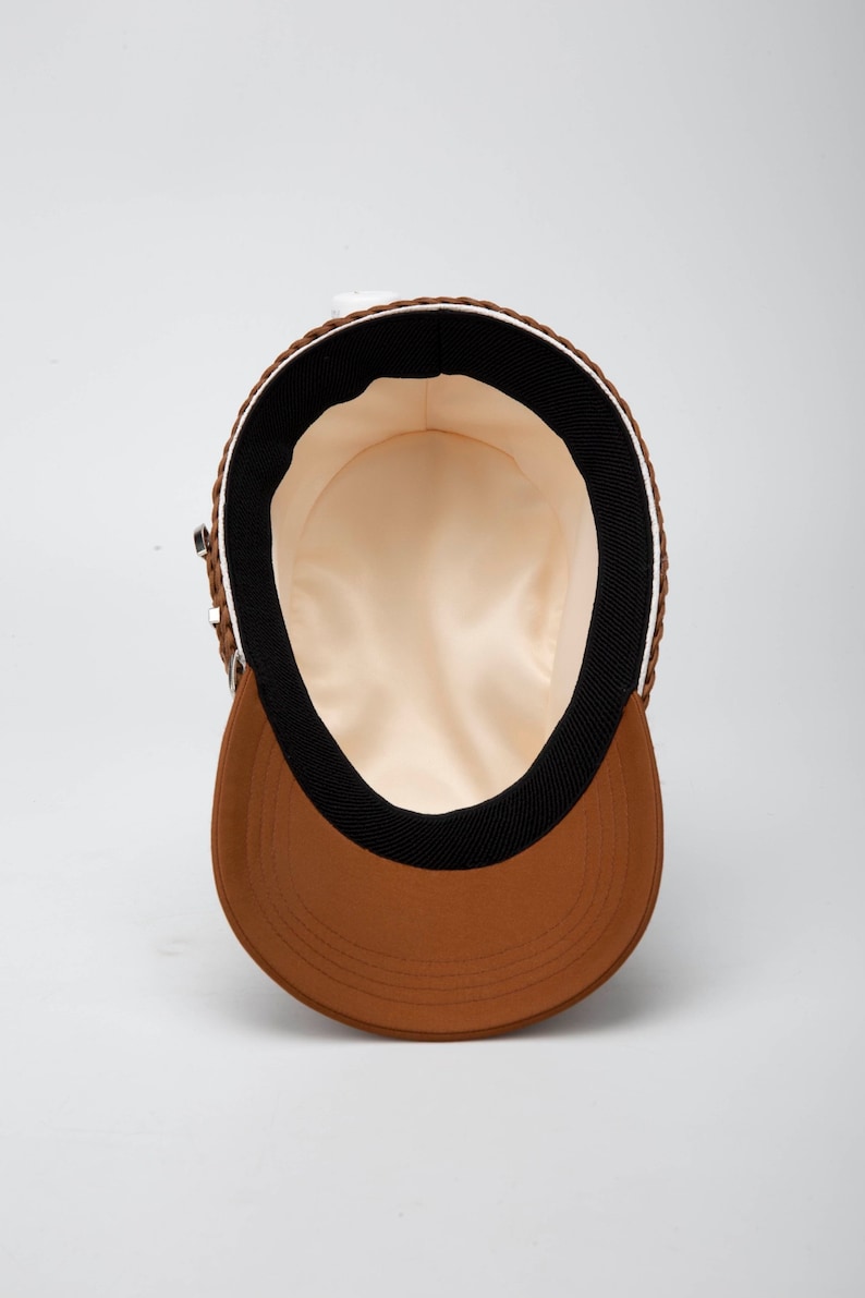 May include: A brown and black baseball cap with a white brim. The inside of the cap is lined with a cream-colored fabric.