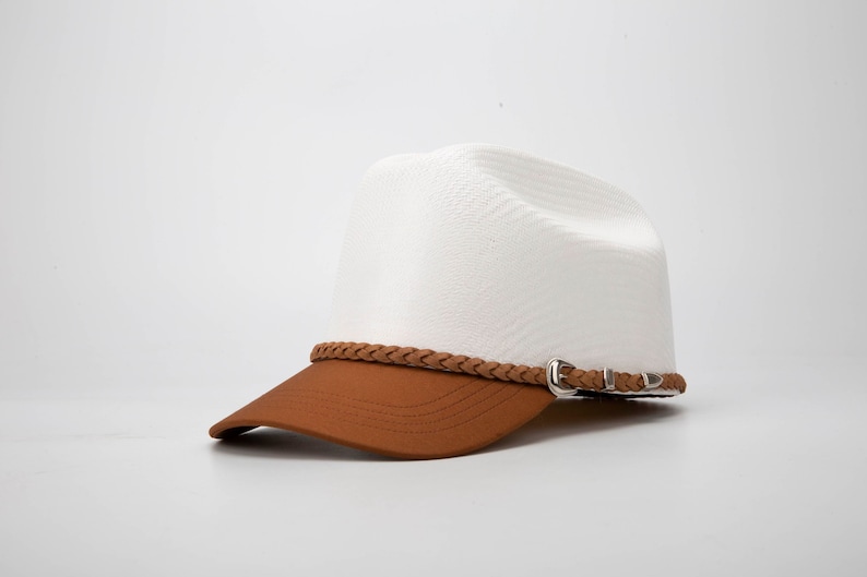 May include: A white and brown baseball cap with a braided leather strap and a silver buckle. The cap has a curved brim and a structured crown.