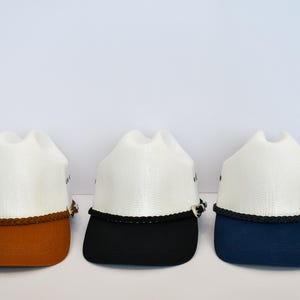 May include: Three white cowboy hats with different colored brims. The hats have a brown, black, and blue brim.