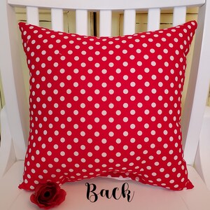 May include: Red pillow with white polka dots. The back of the pillow is shown. The pillow is sitting on a white chair.