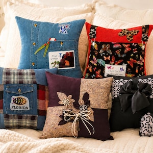 May include: A collection of decorative throw pillows with unique designs. Pillows include denim, plaid, and butterfly patterns. One pillow features a photo and text that reads "Proud Grandpa". Another has a black bow.