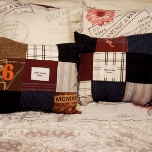 Two patchwork memory pillows with a variety of fabric patterns and colors, including brown, navy, and plaid. One pillow features the number "6" in orange. Both pillows have a personalized label