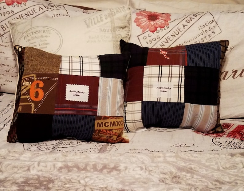 Two patchwork memory pillows with a variety of fabric patterns and colors, including brown, navy, and plaid. One pillow features the number "6" in orange. Both pillows have a personalized label