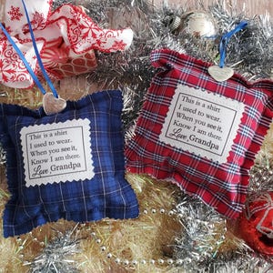 May include: Two square fabric ornaments, one in blue plaid and one in red plaid, each featuring a white patch with the printed text: This is a shirt I used to wear. When you see it, Know I am there. Love, Grandpa. Both hang from blue ribbons.