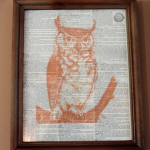 Op de afbeelding: Ingelijste print met een oranje uil-illustratie op woordenboekpagina's. De uil zit op een tak en de lijst is van donkerbruin hout. Een uniek stukje wandkunst.