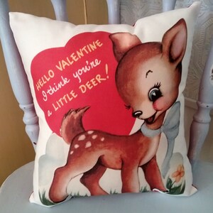 May include: A white pillow with a red heart and a cartoon deer. The heart has the text "HELLO VALENTINE I think you're a LITTLE DEER!" printed on it.