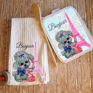 May include: A white kitchen towel and a matching pot holder with a blue and white poodle holding a pink phone in front of the Eiffel Tower. The text "Bonjour" is printed on both items.