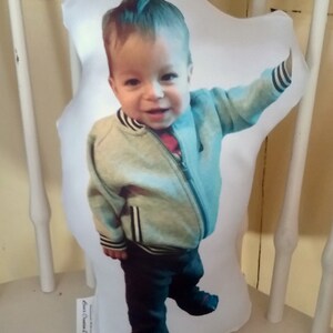 May include: A white pillow with a photo of a young boy wearing a light blue jacket with black stripes and dark blue jeans. The pillow has the text "Aunt's Custom Designs" printed on the bottom.