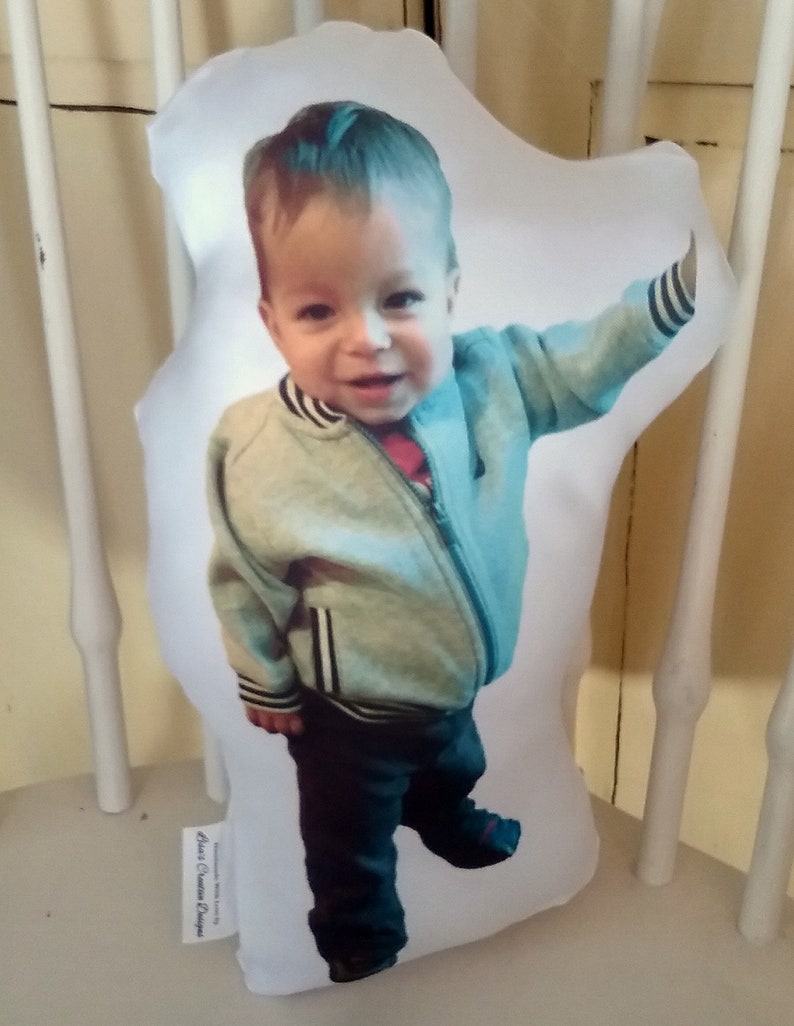 May include: A white pillow with a photo of a young boy wearing a light blue jacket with black stripes and dark blue jeans. The pillow has the text "Aunt's Custom Designs" printed on the bottom.