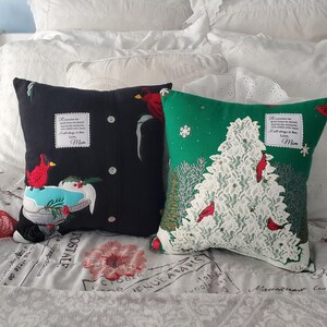 Two decorative memory throw pillows made from Christmas sweaters. One black pillow features a red cardinal and a design resembling a shirt. The other is green with a white lace Christmas tree and red cardinals. Both pillows have text patches that reads "Remember the good times we shared...Love, Mom."