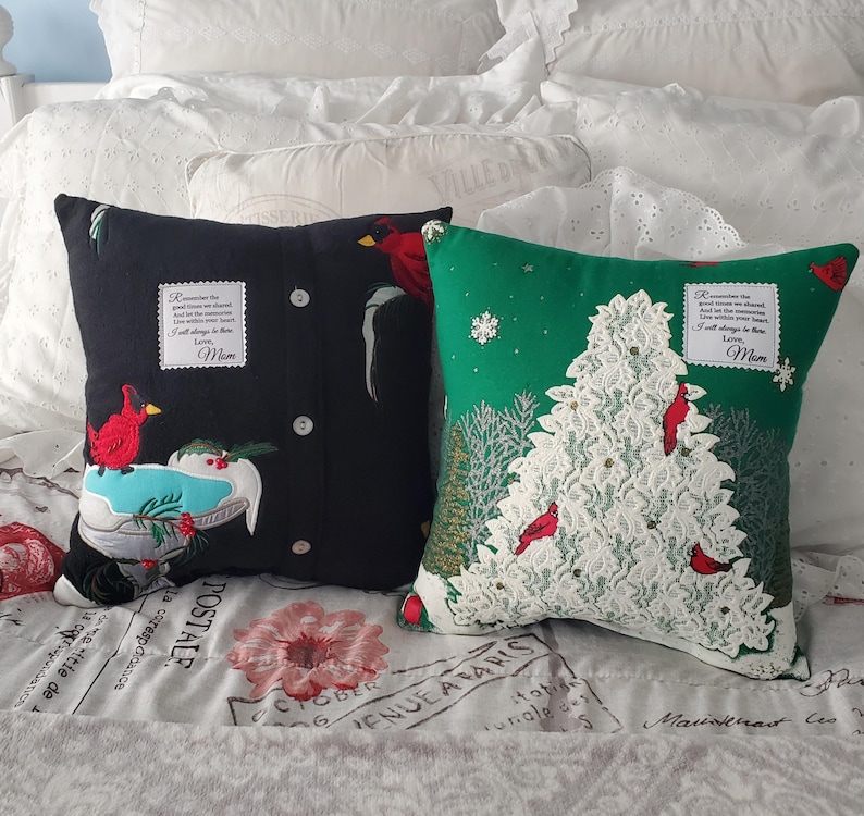 Two decorative memory throw pillows made from Christmas sweaters. One black pillow features a red cardinal and a design resembling a shirt. The other is green with a white lace Christmas tree and red cardinals. Both pillows have text patches that reads "Remember the good times we shared...Love, Mom."