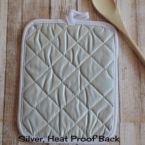 May include: Silver heat-proof pot holder with a quilted design. The back of the pot holder is visible in the image. "Silver, Heat Proof Back" is printed on the bottom edge of the pot holder.