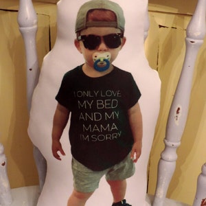 May include: A white pillow with a printed image of a young boy wearing a black shirt, sunglasses, and a blue baseball cap. The shirt has the text "I only love my bed and my mama I'm sorry".