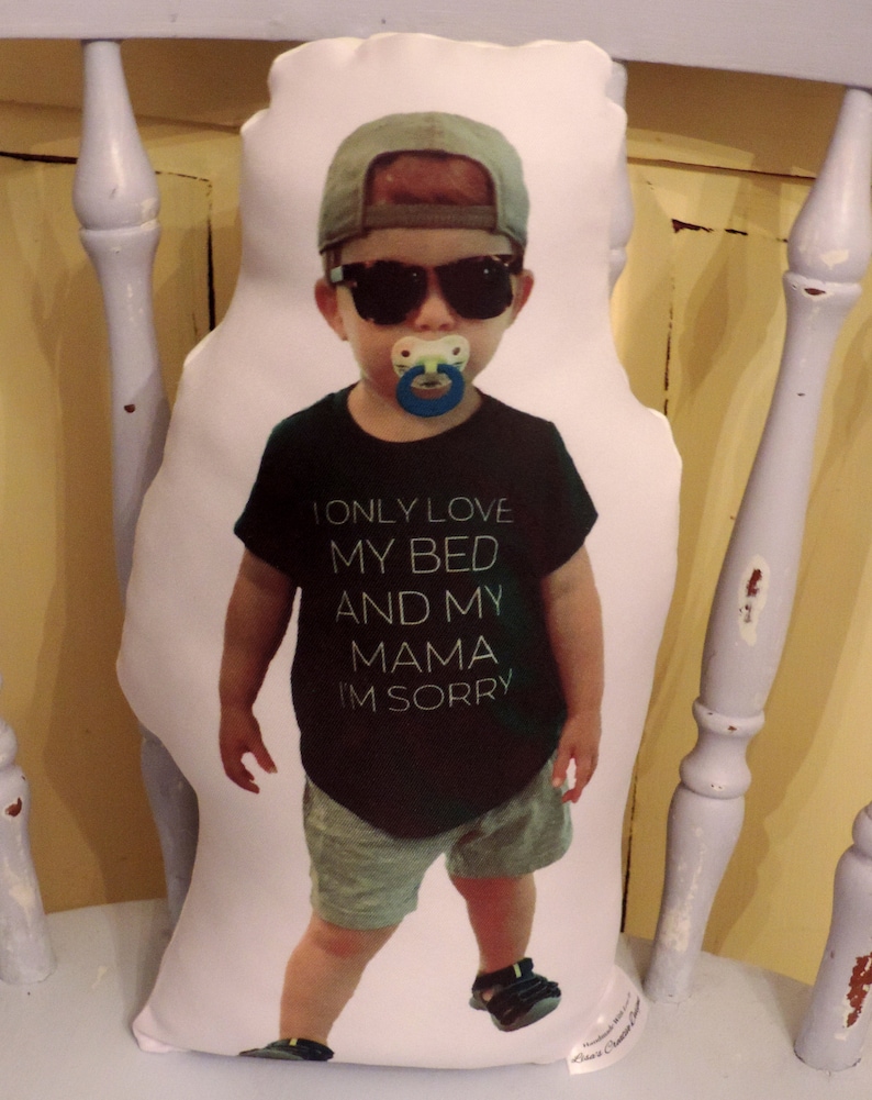 May include: A white pillow with a printed image of a young boy wearing a black shirt, sunglasses, and a blue baseball cap. The shirt has the text "I only love my bed and my mama I'm sorry".