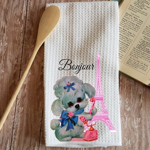 May include: White kitchen towel with a pink Eiffel Tower and a cartoon poodle holding a pink rotary phone. The text "Bonjour" is printed in black above the Eiffel Tower.