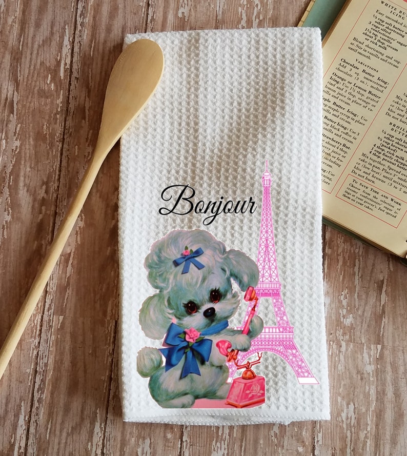 May include: White kitchen towel with a pink Eiffel Tower and a cartoon poodle holding a pink rotary phone. The text "Bonjour" is printed in black above the Eiffel Tower.
