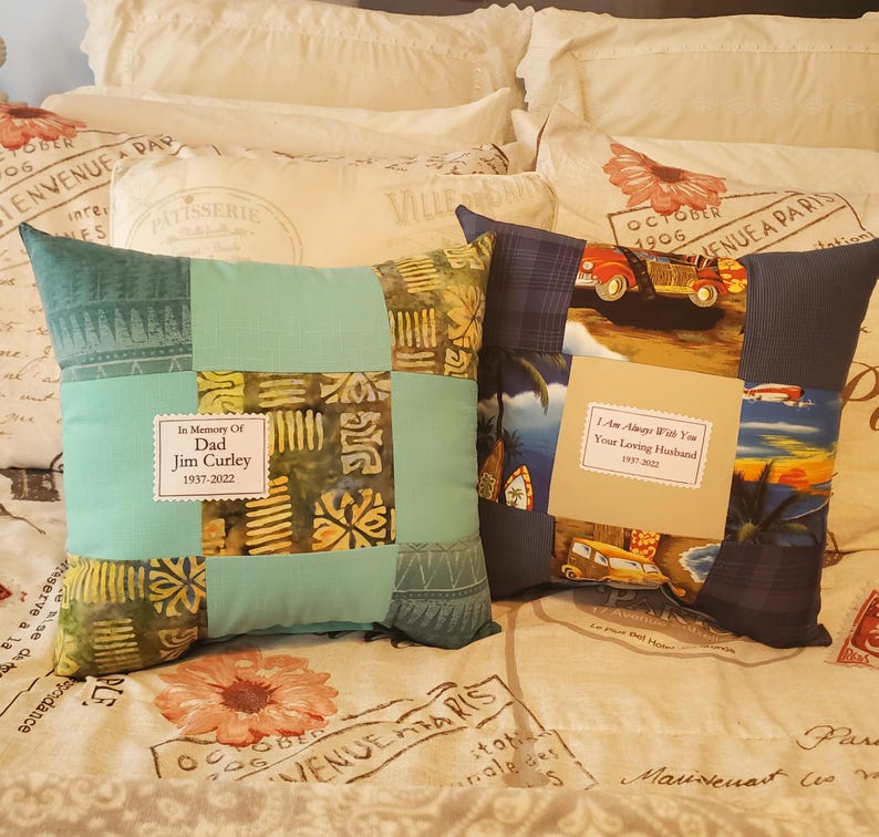 Two decorative memory throw pillows with patchwork designs. One pillow features a teal and patterned fabric with a label. The other pillow has a vintage car print and a label.