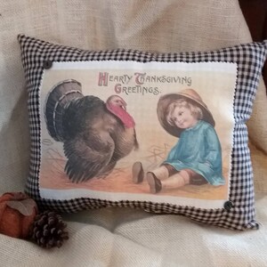 May include: Thanksgiving-themed pillow with a vintage illustration of a turkey and a child. The pillow has a black and white checkered border and the text "Hearty Thanksgiving Greetings."