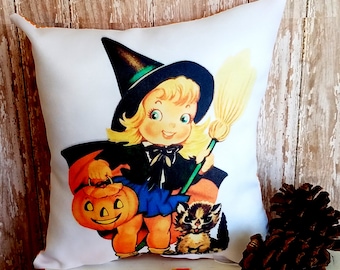 May include: White square Halloween throw pillow featuring a vintage illustration of a smiling witch holding a jack-o'-lantern and broom, with a raccoon. The witch wears a black hat and cape, with a blue skirt. Candy corn is scattered in the foreground.