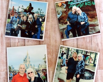 May include: Four square ceramic coasters with different family photos printed on them. The photos show a family at Disney World, including a photo in front of Cinderella's Castle, a photo in front of a large green tree, a photo in front of a fountain, and a photo in front of a sign that says "A wild place to shop and eat".
