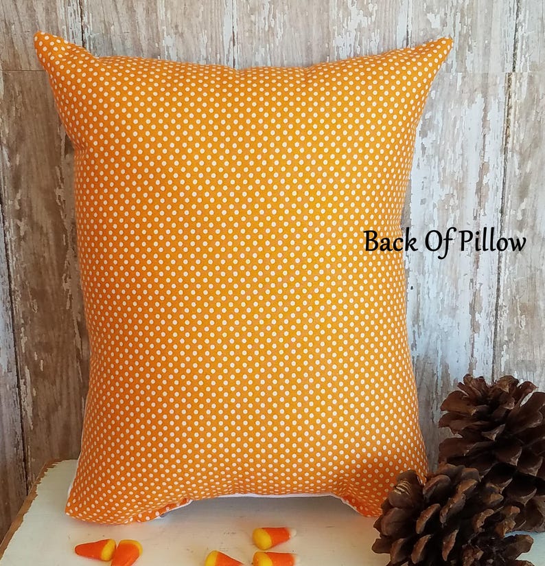 May include: An orange pillow with white polka dots. The pillow has a unique shape with pointed corners. The text "Back Of Pillow" is visible on the pillow. Candy corn and pine cones are in the foreground.
