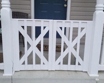 May include: A white wooden gate with an X-shaped design, flanked by white support posts. The gate is closed, and the background includes a blue door and a welcome mat.