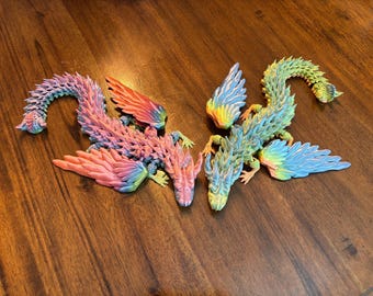 May include: Two colorful, articulated dragon figurines with rainbow gradients. The dragons have detailed scales and wings, and are posed on a wooden surface. The color palette includes pink, blue, yellow, and green.