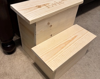 May include: A two-step wooden pet step stool. The natural wood-colored stool has the name "Evie" and paw prints engraved on the top step. The step stool is designed to help pets reach higher places.