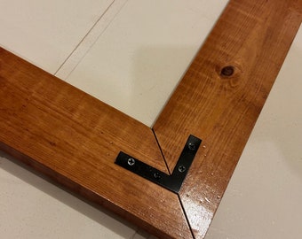 May include: Close-up of a corner joint of a wooden frame with black metal corner brackets. The wood is stained a dark brown color.