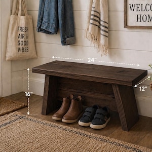 May include: A dark brown wooden bench, 24 inches long, 16 inches high, and 12 inches deep, with shoes underneath. A tote bag with "FRESH AIR & GOOD VIBES" hangs nearby. A sign says "WELCOME HOME". A basket with a plant and a "BE KIND" tag is also present.