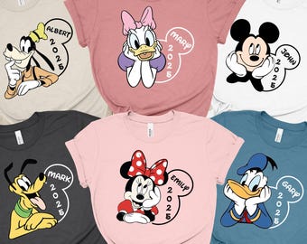 May include: Six different t-shirts featuring Disney characters, including Mickey Mouse, Minnie Mouse, Donald Duck, Goofy, and Pluto. Each shirt has a different character and a name and year printed on it. The shirts are all in different colours, including pink, white, blue, grey, and beige.