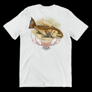 May include: White t-shirt featuring a detailed illustration of a redfish. The fish is brown and gold with blue and orange fins, set against a faded gold and brown background. The shirt includes the text "BANDIT" in a stylized font.