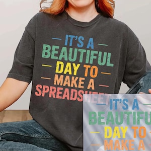May include: Dark gray t-shirt with the text "IT'S A BEAUTIFUL DAY TO MAKE A SPREADSHEET" in colorful letters. A DTF transfer of the same design is also visible.