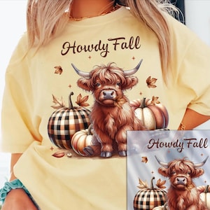 May include: A pale yellow t-shirt featuring a graphic print of a brown Highland cow sitting among pumpkins. The text Howdy Fall is printed in brown above the cow. Some pumpkins have a black and white plaid pattern, and brown autumn leaves are scattered around the design.