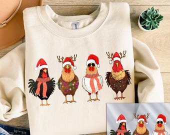 May include: A cream-colored crewneck sweatshirt featuring a graphic of four chickens wearing Santa hats, scarves, and reindeer antlers, with some adorned in colorful Christmas lights. The design is printed on the front of the garment.