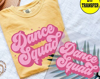 May include: Mustard yellow t-shirt with the words "Dance Squad" in pink, retro-style lettering. A DTF transfer with the same design is visible. The shirt has a crew neck and short sleeves.