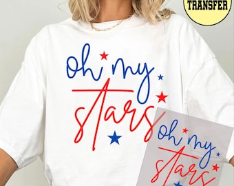 May include: White t-shirt with the phrase "Oh My Stars" in blue and red script, accented with stars. A DTF transfer is visible in the upper right corner. The shirt is a casual style.