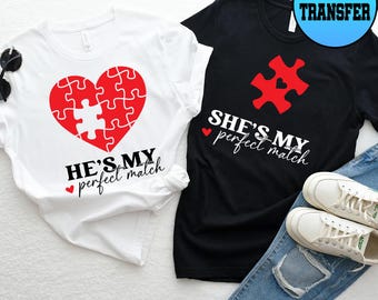 Puede incluir: Dos camisetas, una blanca y otra negra, con diseños a juego. La camiseta blanca presenta un corazón rojo hecho de piezas de rompecabezas con el texto "HE'S MY perfect match". La camiseta negra tiene una pieza de rompecabezas roja con el texto "SHE'S MY perfect match".