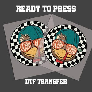 May include: Two DTF transfer sheets with a cartoon turkey wearing sunglasses that say "GOBBLE". The turkey has a teal cap and a checkered background. The text "READY TO PRESS" and "DTF TRANSFER" are above and below the images.
