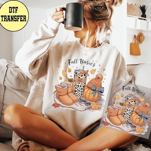 May include: Cream-colored sweatshirt with a fall-themed graphic. The graphic includes a leopard print tumbler, pumpkin, boots, and the text "Fall Basics". A DTF transfer logo is in the upper left corner.