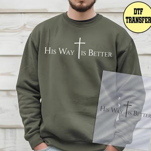May include: Olive green sweatshirt with the text "His Way Is Better" and a white cross graphic. The design is centered on the chest. The sweatshirt is a crew neck style.