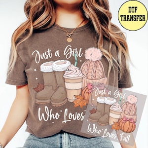 May include: Brown t-shirt with the text "Just a Girl Who Loves Fall." The graphic includes illustrations of boots, a coffee drink, a knit hat with a pom-pom, and a pumpkin. The image is a DTF transfer.