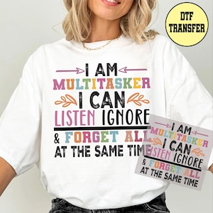 May include: White t-shirt with the text "I AM MULTITASKER I CAN LISTEN IGNORE & FORGET ALL AT THE SAME TIME" in various colors. A DTF transfer is visible in the upper right corner.