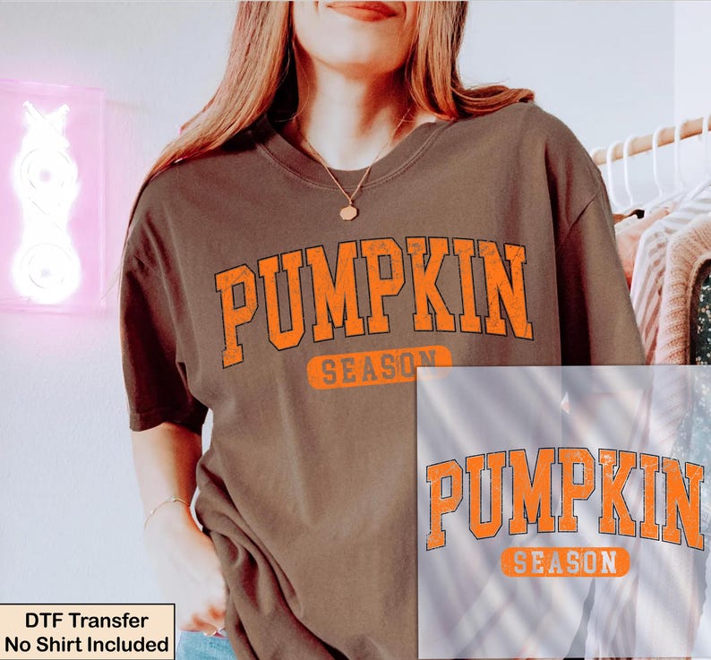 K&ouml;nnte beinhalten: Ein dunkelbraunes Kurzarm-T-Shirt mit dem Text PUMPKIN SEASON in einer abgenutzten orangefarbenen College-Schriftart auf der Brust. Das Shirt hat einen Rundhalsausschnitt und eine lockere Passform. Der Text DTF Transfer No Shirt Included ist unten links zu sehen.