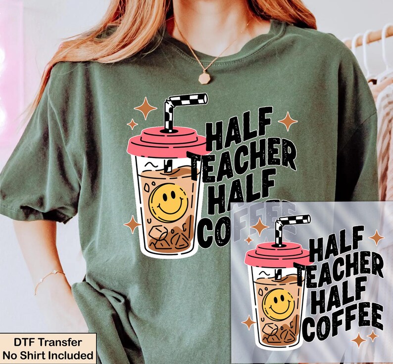 May include: A dark olive green t-shirt featuring a graphic of an iced coffee cup with a pink lid, a checkered straw, and a yellow smiley face. The text reads HALF TEACHER HALF COFFEE, accompanied by small four-pointed star icons in a light orange color.