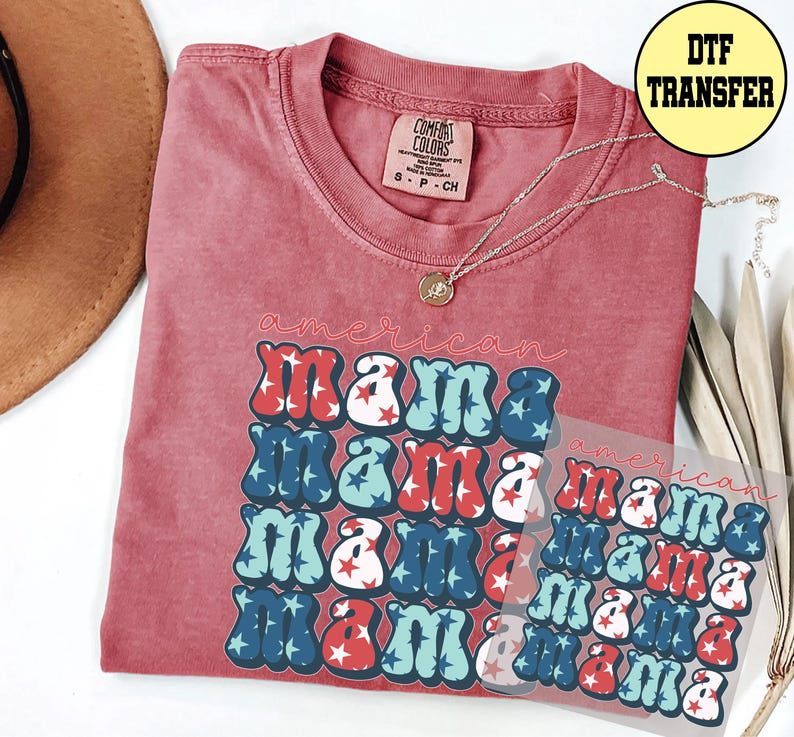 May include: A red t-shirt with the words "american mama" in a retro font, with red, white, and blue stars. A DTF transfer is visible. A gold necklace is draped on the shirt.