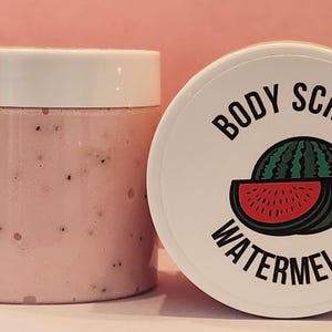 Op de afbeelding: Een witte pot met een roze lichaamsscrub erin. De pot heeft een wit deksel met de tekst "BODY SCRUB WATERMELON" erop gedrukt. Een watermeloen-schijf-afbeelding is ook op het deksel gedrukt.